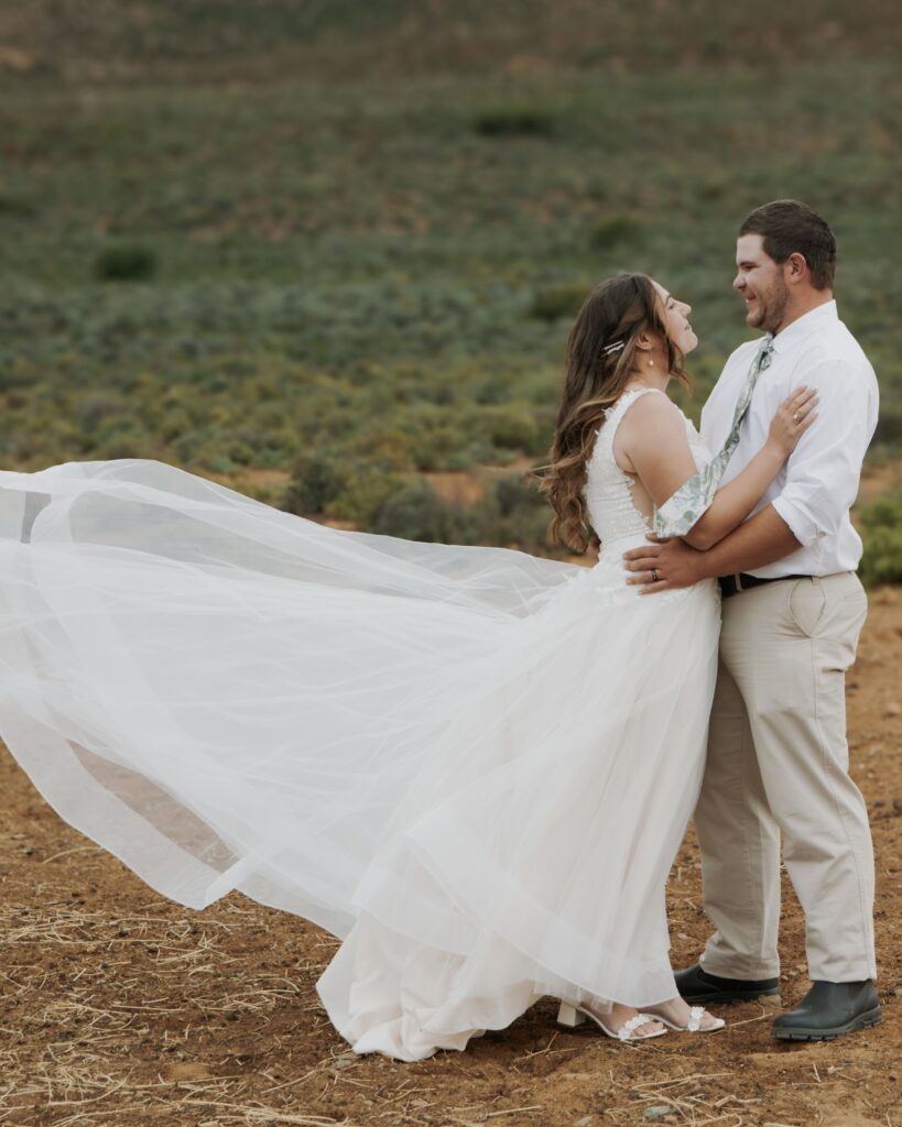 Newly weds in a field with the brides dress blowing in the wind